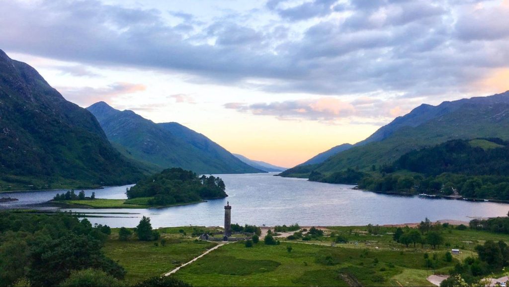 A sunrise above grassy flats, green mountains and a blue loch in the Scottish Highlands. Photo: Katia De Juan